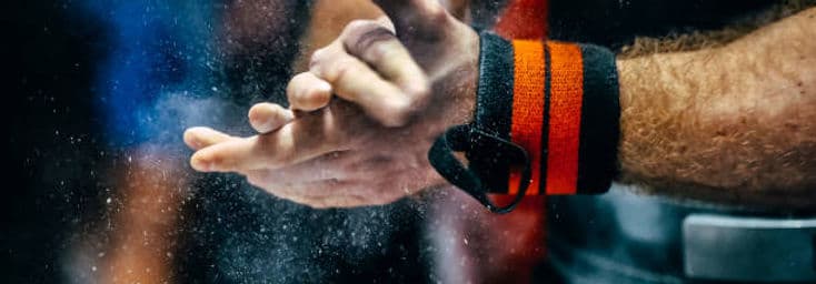 Chalk dust comes off a lifter's hands above the bar, wrist wraps already on.