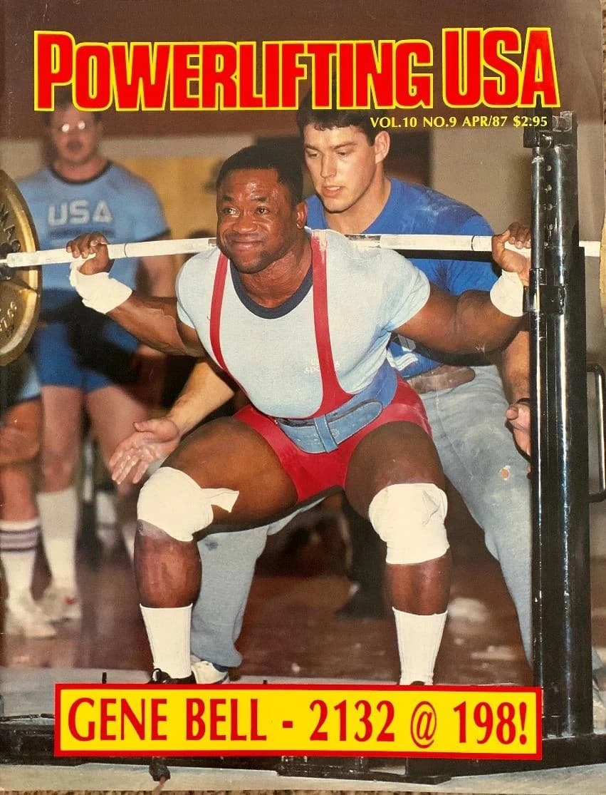 Powerlifting USA cover from April 1987: a lifter at the bottom of a squat with a spotter tracking the bar behind him.