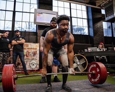 A lifter sets his back over a loaded bar at the start of a deadlift attempt.