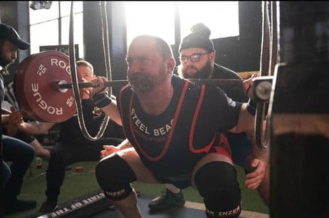 A lifter in a Steel Beach singlet drives out of the bottom of a squat.