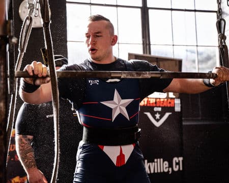 A lifter in a star-fronted singlet settles under the bar before walking a squat out of the rack.
